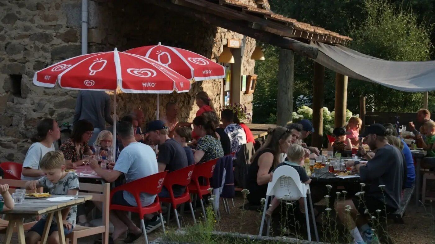 Een buitenruimte met een eethoek, rode stoelen en tafels, stenen muren en een overdekt gedeelte met een witte luifel.