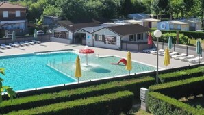 Una piscina con tobogán, rodeada de sillas de descanso y sombrillas, con casas y colinas al fondo.