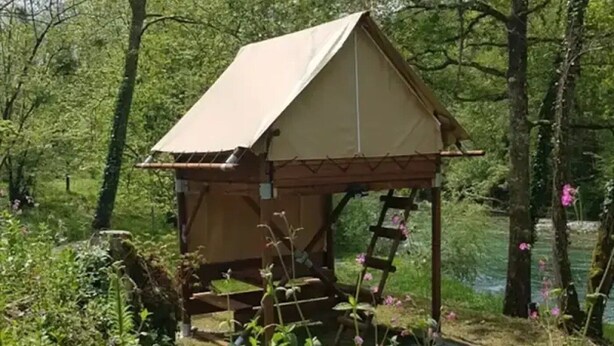 Une petite construction en bois, dotée d’un toit à deux versants, entourée de verdure et de fleurs.