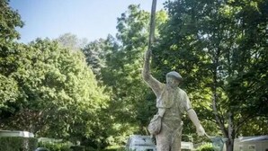 Une statue représentant un homme tenant un drapeau, entourée de verdure et d’une pancarte sur laquelle on peut lire « LE PÊCHEUR ».