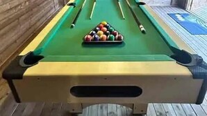 Une table de billard avec les billes au centre, entourée de murs en bois et recouverte d’un plancher en bois.