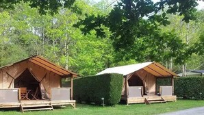 Twee houten chalets met schuine daken, elk met een klein terrasje en een tafel.