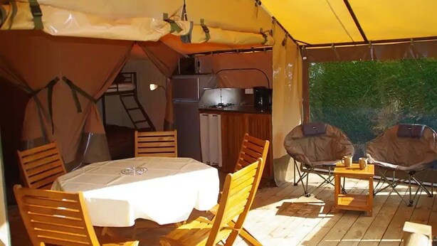 Een tentaccomodatie met een tafel, stoelen, een kitchenette en uitzicht op groen.