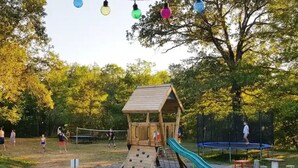 Een speeltuin met een houten speelhuisje, een glijbaan en een trampoline.