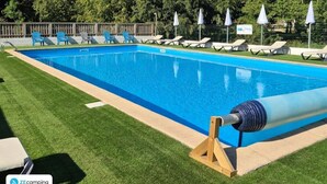Piscina com espreguiçadeiras e guarda-sóis, cercada por uma vedação de madeira e árvores.