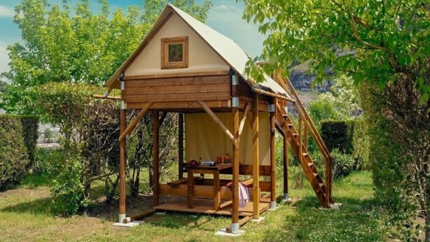 Uma cabana de madeira com telhado inclinado, uma pequena janela e uma escada que leva a uma plataforma.