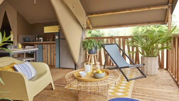 Un espacio al aire libre acogedor con un sofá, una butaca, una mesa de fibra natural y una planta en maceta.
