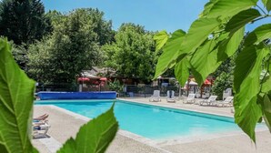 Piscina con sillas de descanso y sombrillas, rodeada de árboles y una cerca.