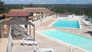 Una piscina con sillas de descanso, una zona cubierta y edificios al fondo.