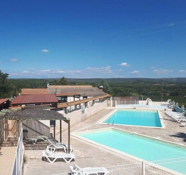 Une piscine avec des chaises longues, un espace abrité et des bâtiments en arrière-plan.