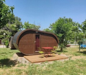 Une structure en bois avec une porte rouge, un petit patio avec une table et des chaises, et une zone herbeuse environnante.