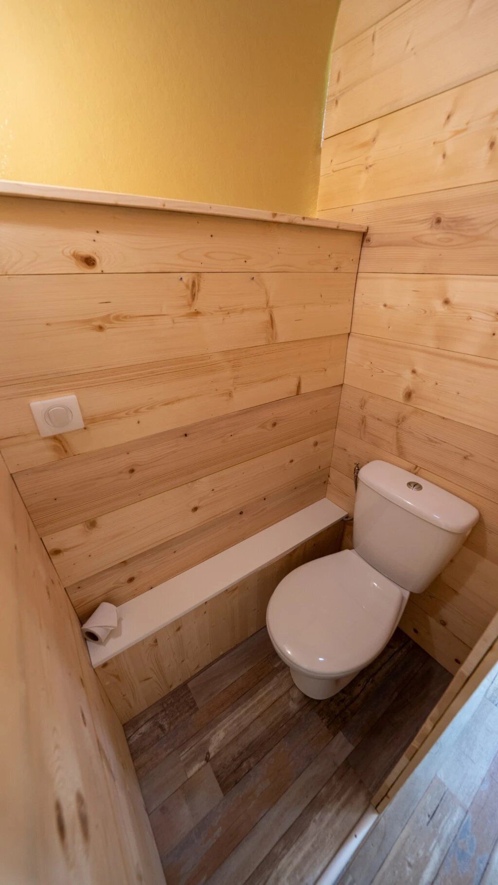 Un bagno piccolo, con rivestimenti in legno, un WC e un pavimento in legno.