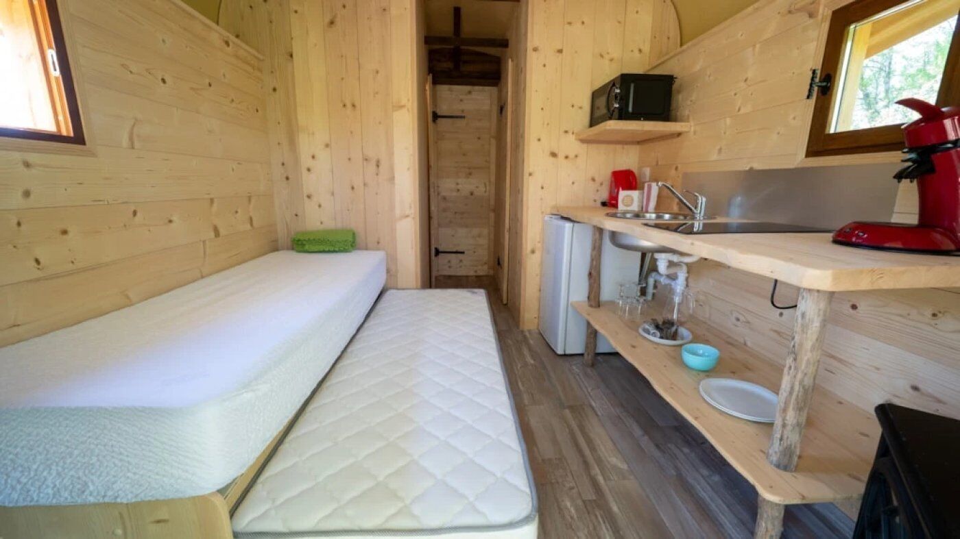 A compact wooden cabin with a bed, a small kitchenette, and a window.