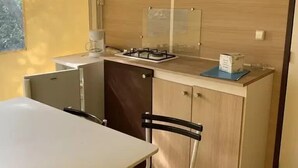 Pieni, käytännöllinen keittiö, jossa on kaasuliesi, pieni jääkaappi ja puinen kaappi.