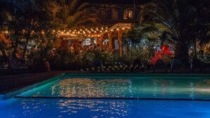 A nighttime pool area with a clear water surface, surrounded by palm trees and a building with string lights. - ZEcamping 3 étoiles piscine animaux acceptés tente 12m2 2 pers (Tuchan)