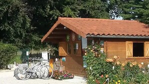 A wooden building with a tiled roof, bicycles parked in front, and a flower bed with various flowers. - ZEcamping 3 étoiles piscine couverte locatif BBQ 4 pers (Sandrans)