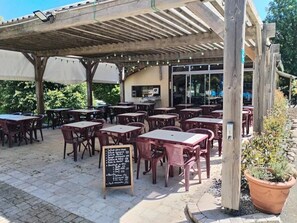 Ein Straßencafé mit Holztischen und -stühlen, einem überdachten Sitzbereich und einer Kreidetafel als Speisekarte.
