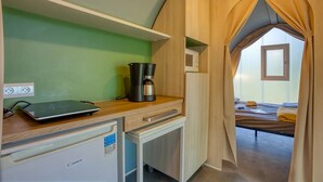 Et lille tekøkken med kaffemaskine, computer og køleskab.