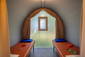 Ein schmales Zimmer mit zwei Betten, einem Fenster und einer Tür.