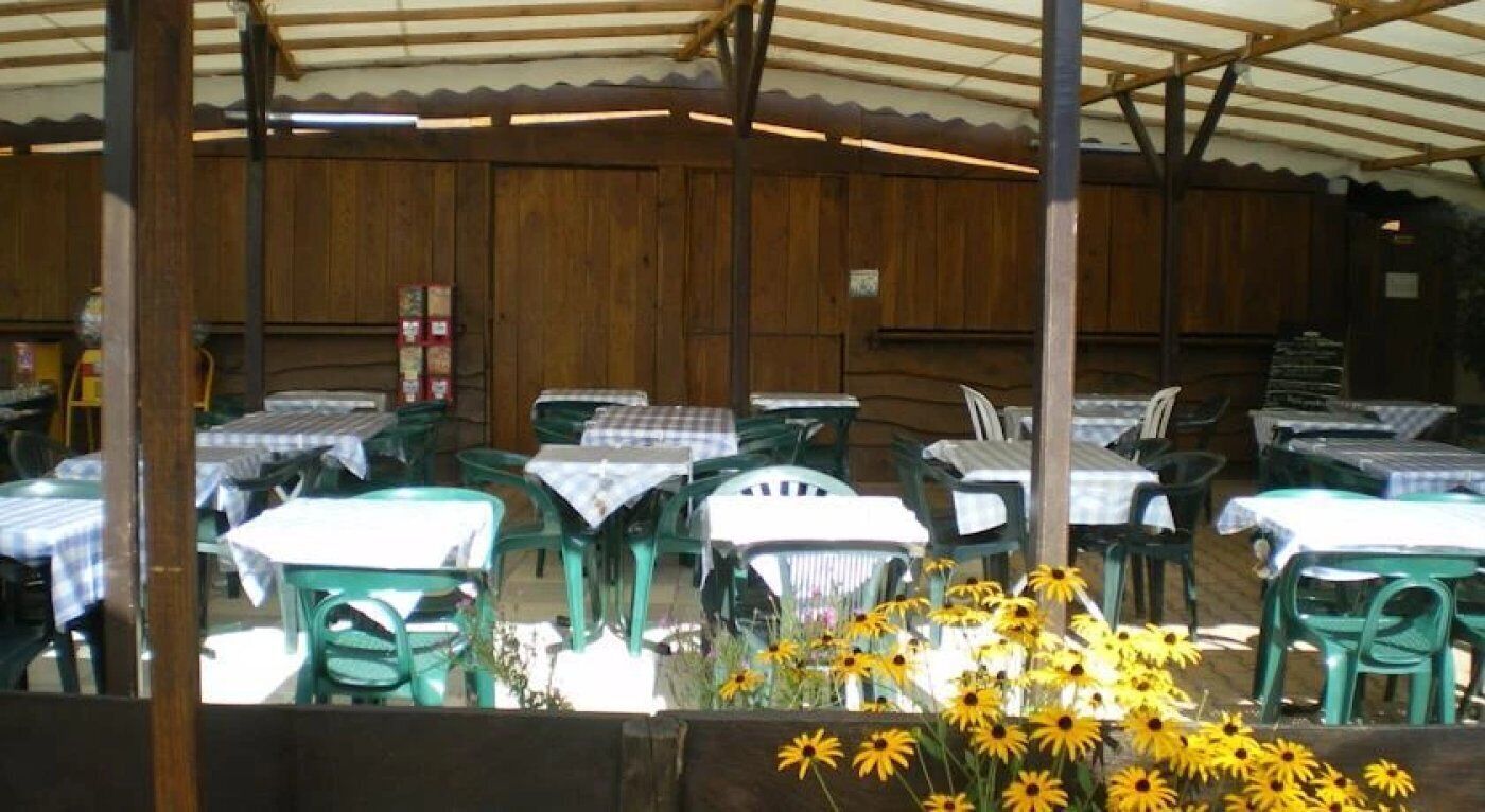 Un área de comedor al aire libre con mesas y sillas, cubierta por una estructura de madera.