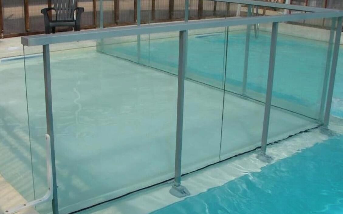 A swimming pool with a glass barrier and metal support columns.