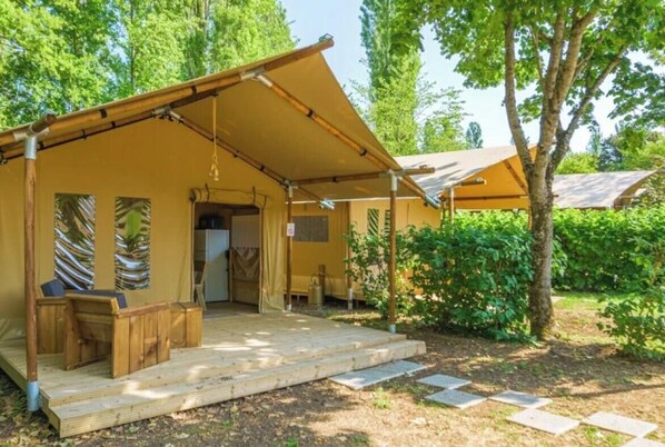 Un hébergement sous tente doté d’un espace extérieur couvert avec des sièges, d’une terrasse en bois et situé dans un cadre verdoyant.