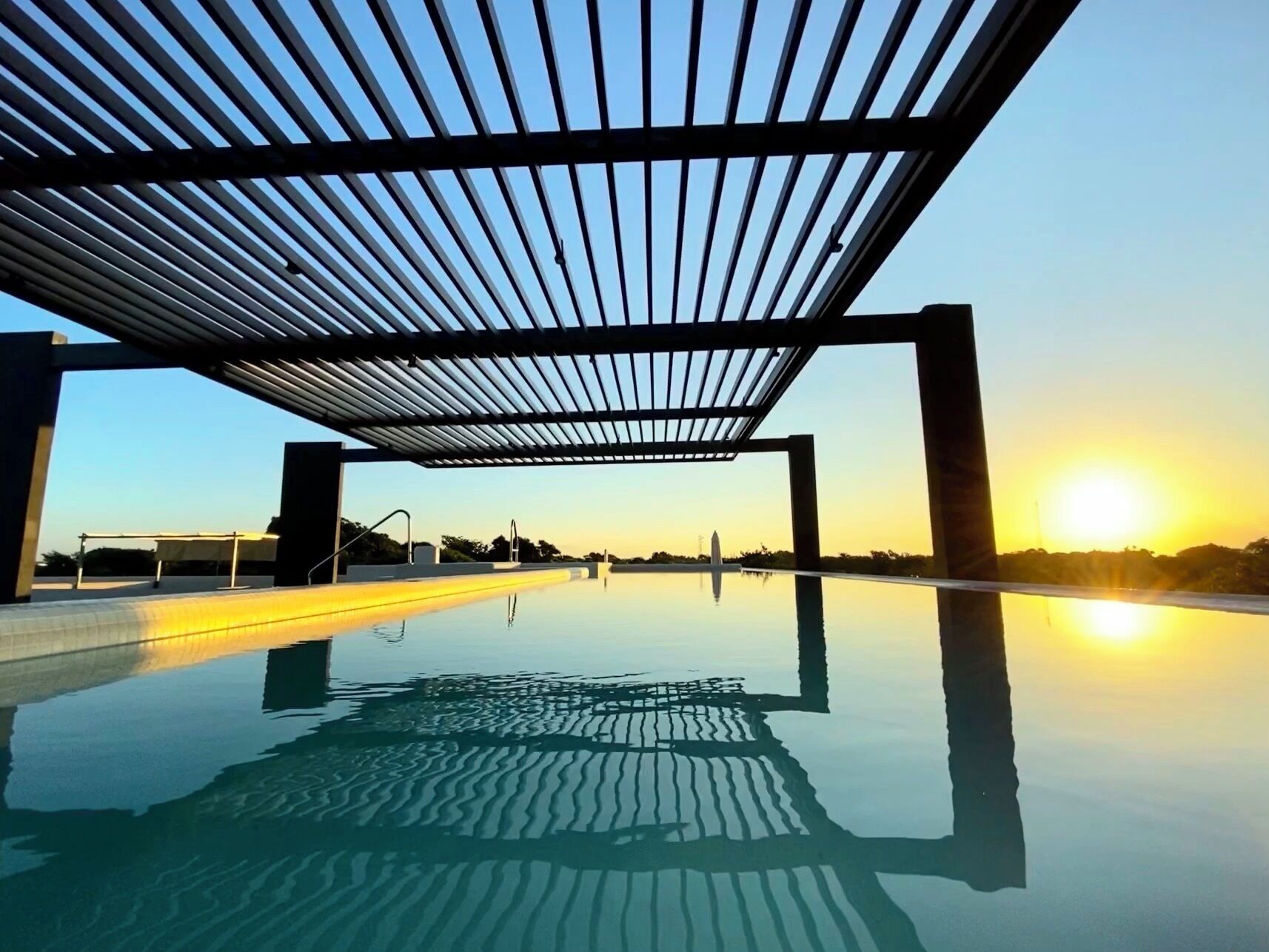 Ein klarer Blick auf ein Infinity-Pool mit moderner Pergola, die Himmel und Sonne reflektiert.