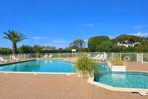 Une piscine rectangulaire entourée d’une clôture blanche, avec des chaises longues et des palmiers tout autour.