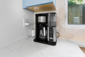 A kitchen with a coffee maker, a white cup, and a window with a view of a fence. - Modern suite | Mins from DT Raleigh | Ground Floor (Raleigh)