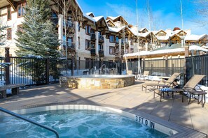A pool area with a hot tub, lounge chairs, and a stone fountain.