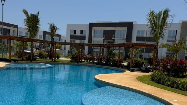 A swimming pool with a wooden deck, surrounded by modern buildings and palm trees. - Depa Coral- Luxory apartment with Private Beach Club (Acapulco de Juárez)