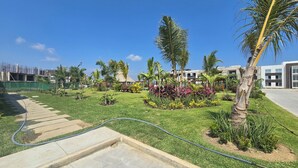A well-maintained garden with palm trees, a concrete pathway, and a building in the background. - Depa Coral- Luxory apartment with Private Beach Club (Acapulco de Juárez)