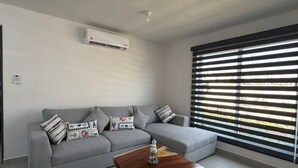 A modern living room with a grey sofa, a wooden coffee table, and a large window with horizontal blinds. - Depa Coral- Luxory apartment with Private Beach Club (Acapulco de Juárez)