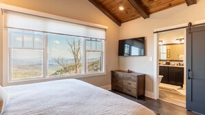 Un dormitorio con una ventana grande, una cama, un aparador y un televisor montado en la pared.