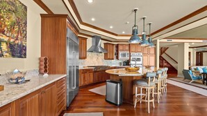 Eine geräumige Küche mit Holzausbau, einem Edelstahlkühlschrank, einem Gasherd und einer großen Kücheninsel mit Barhocker.