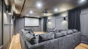 Un cine en casa con un sofá modular grande, una pantalla de proyector y piso de madera.