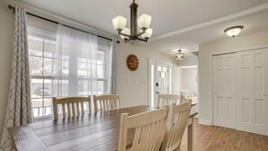 Un comedor con mesa y sillas de madera, una araña y vistas al exterior a través de amplios ventanales.