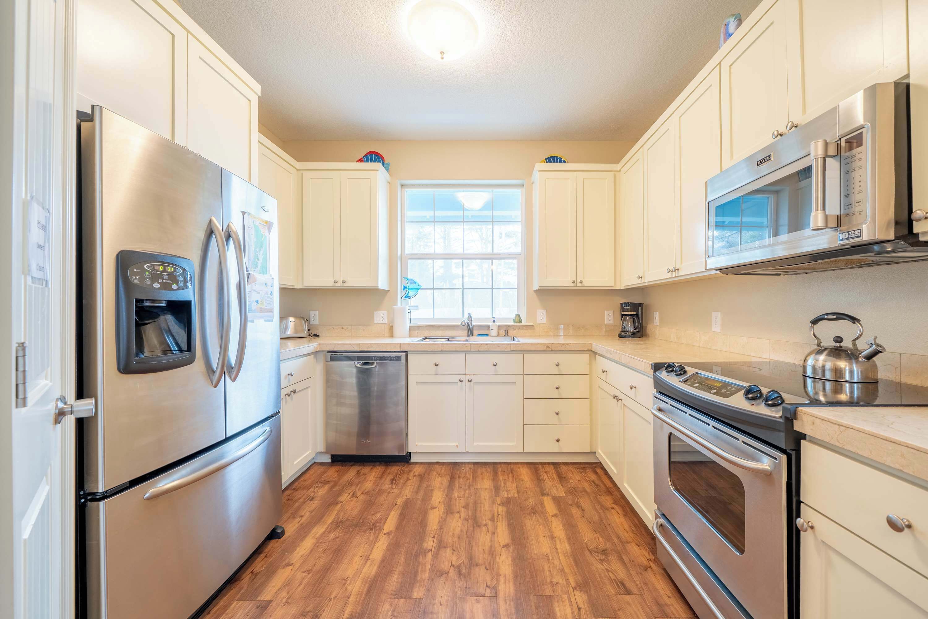 A kitchen with stainless steel appliances, wooden flooring, and white cabinetry.