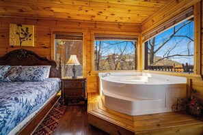 Ein Schlafzimmer einer Holzhütte mit einem großen Bett, Holzboden, einem Fenster mit Aussicht und einer Badewanne.