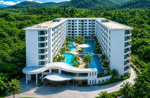 Ein modernes Hotel mit einem zentral gelegenen Schwimmbad, umgeben von üppiger Vegetation und einer Bergkulisse.