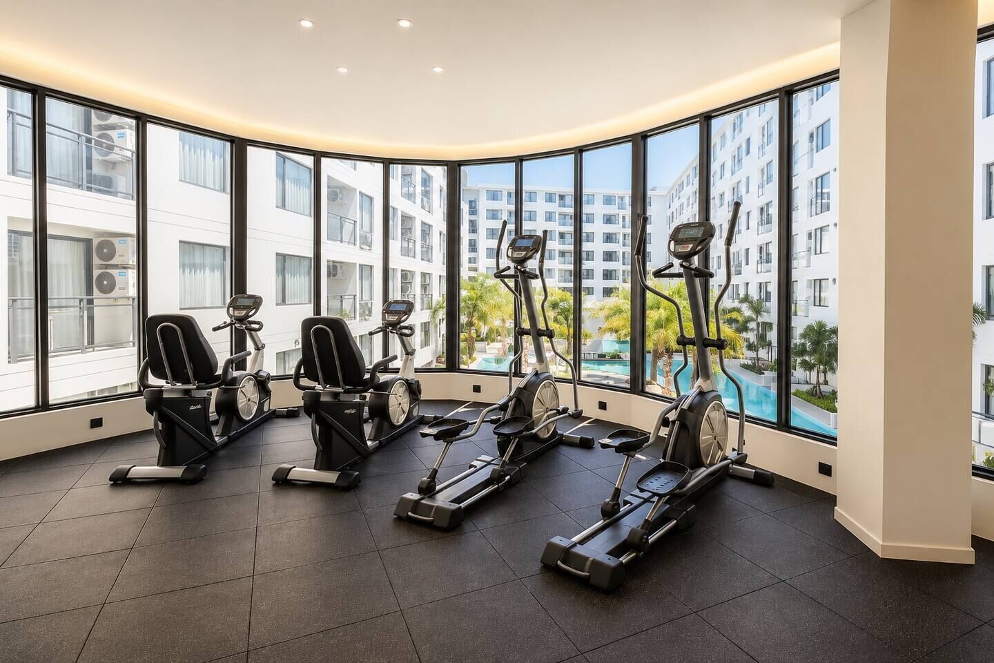 Un gimnasio con equipo de ejercicio y amplias ventanas con vistas a una piscina y edificios.