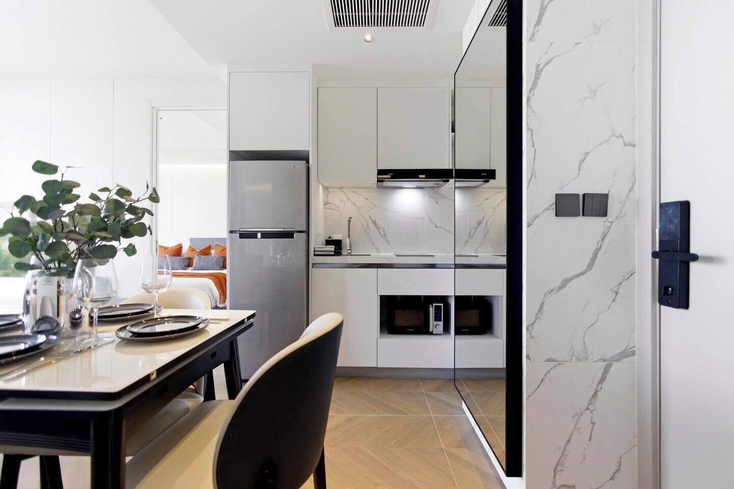 Uma cozinha moderna com frigorífico, micro-ondas e forno embutidos, e um espaço de refeições com mesa posta para dois.