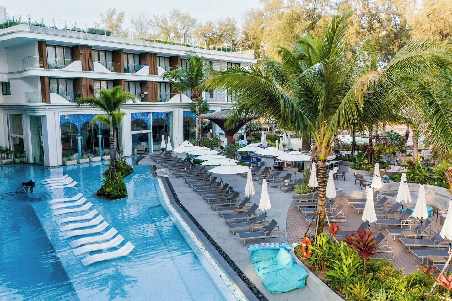 A hotel with a swimming pool, sun loungers, and palm trees.