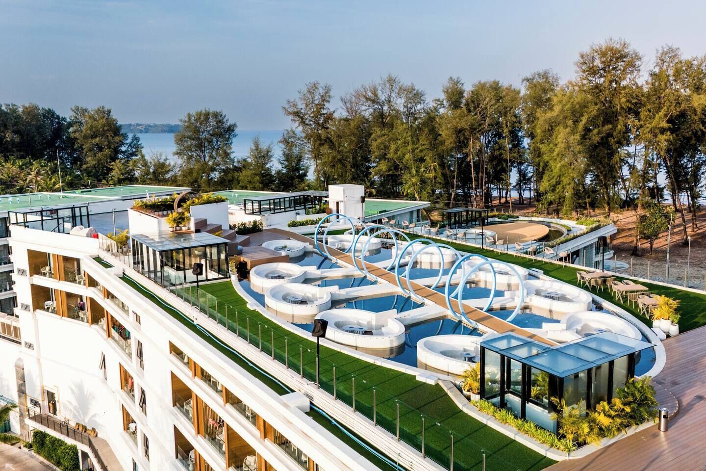 A hotel with multiple swimming pools, a tennis court, and a view of the sea.