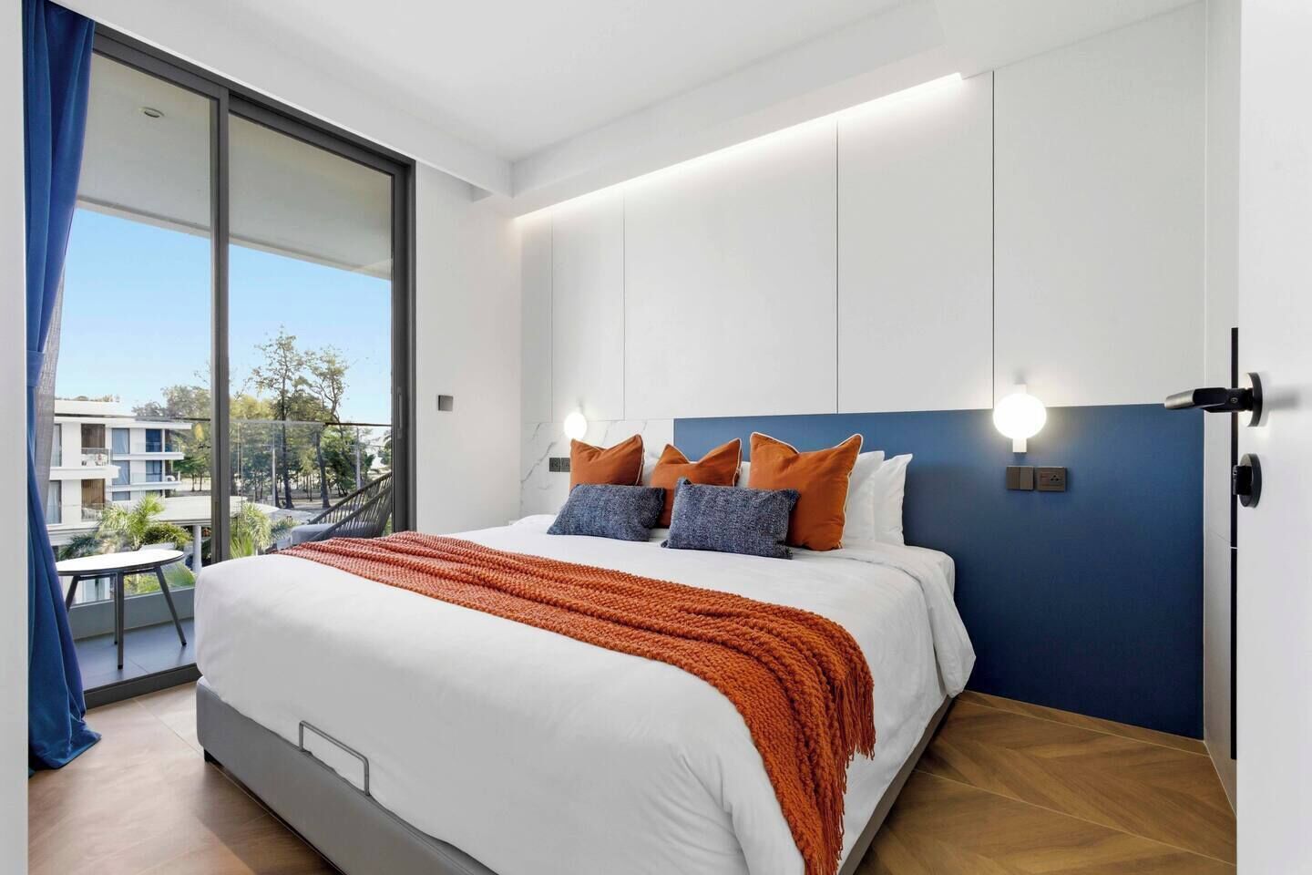 Una habitación de hotel moderna con una cama grande, un balcón con vistas y una lámpara de techo luminosa.