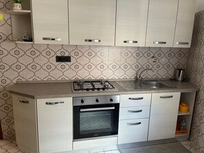 Eine Küche mit Gaskochfeld, Backofen, Spüle und einer Wandfliesenverkleidung mit Muster.