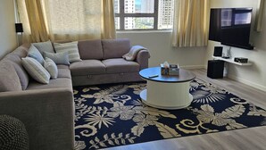 A living room with a sofa, a coffee table, a TV, and a large window with curtains. - Waikiki  beach is just across  street. (Honolulu)