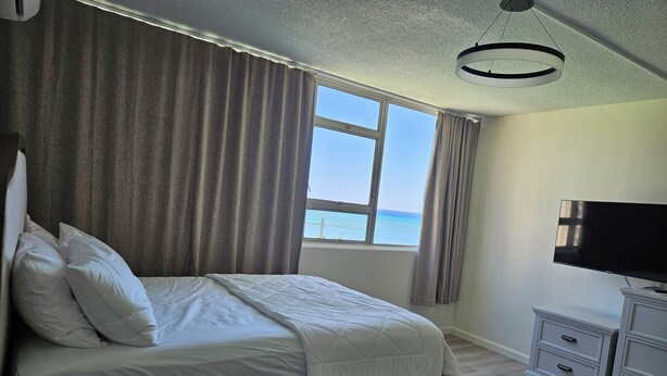 A bedroom with a bed, curtains, a television, and a view of the sea. - Waikiki  beach is just across  street. (Honolulu)