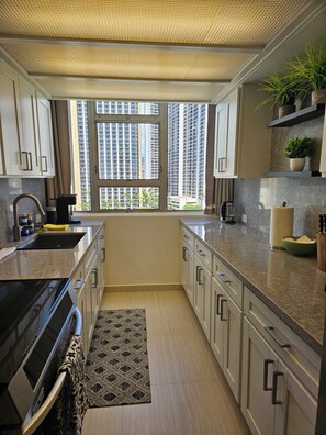 A modern kitchen with a large window, built-in cabinets, a countertop, and a stove. - Waikiki  beach is just across  street. (Honolulu)