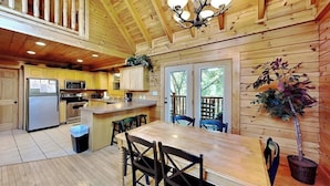 A wooden cabin interior with a dining area, kitchen, and a balcony with a view. - Budget friendly, Smoky Mountain Cabin Rental | Sleeps 10 | Pool Table (Pigeon Forge)